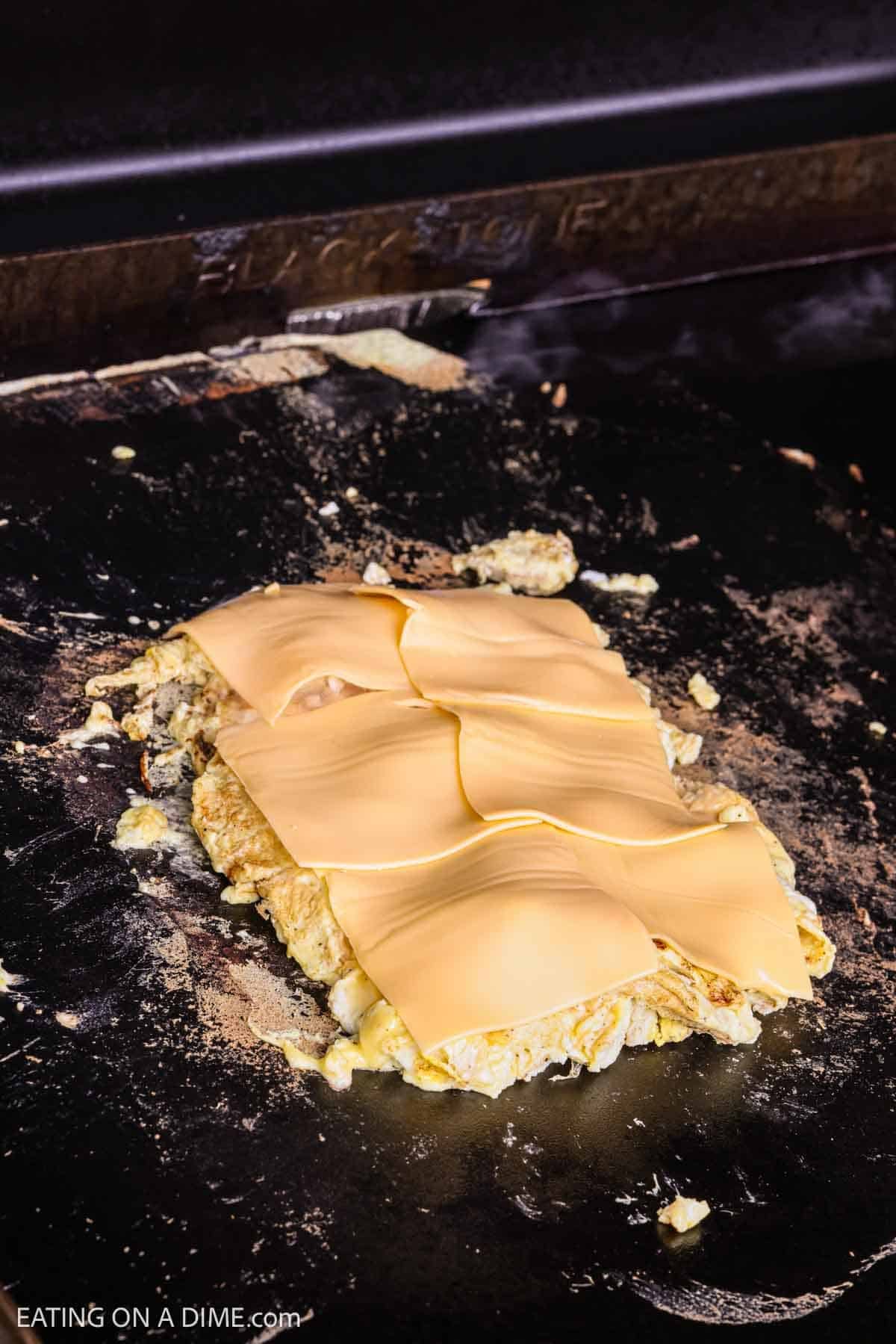 Slice cheese topped on scrambled eggs on a Blackstone Griddle. 