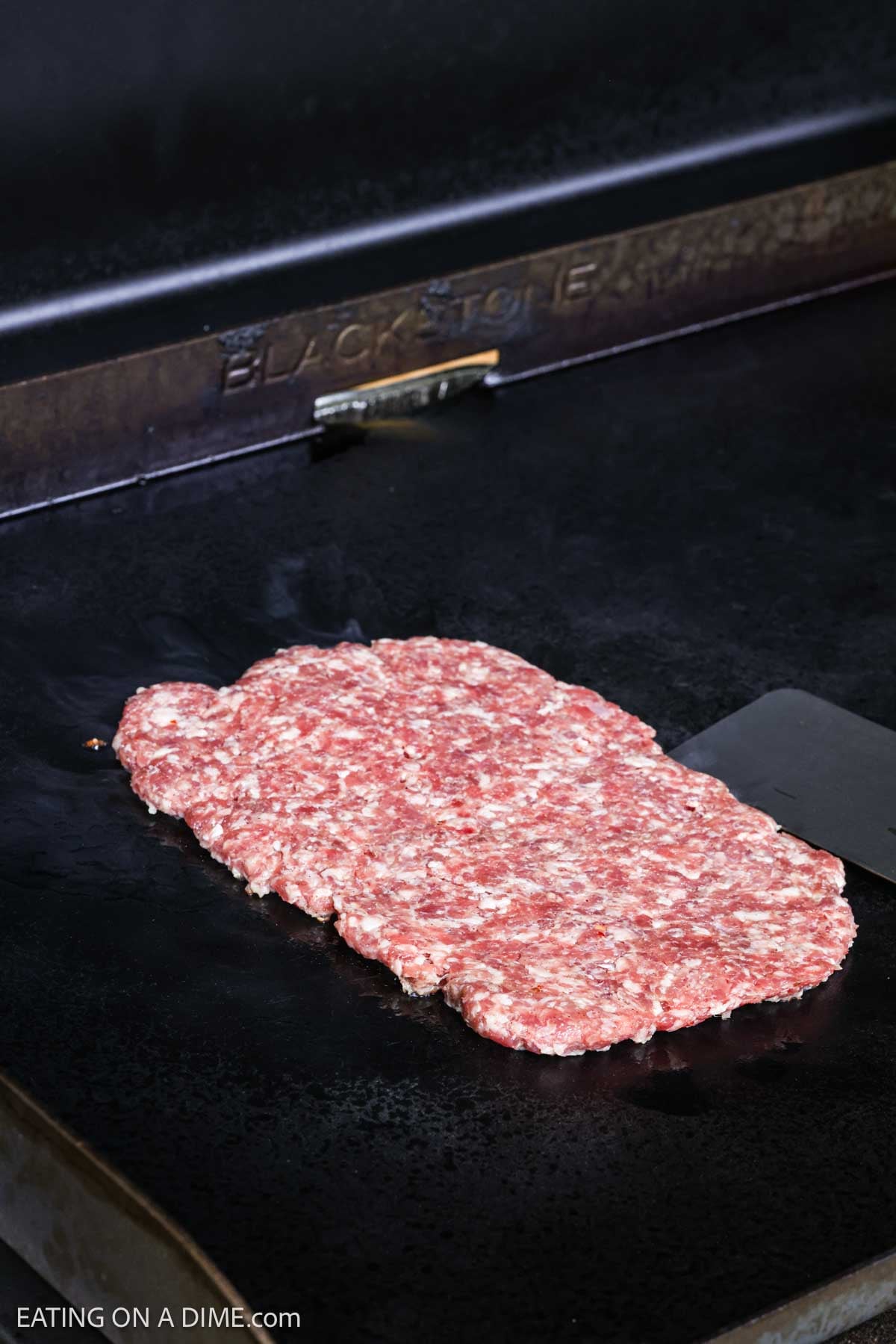 Sausage flatten into a rectangle cooking on a Blackstone Griddle. 