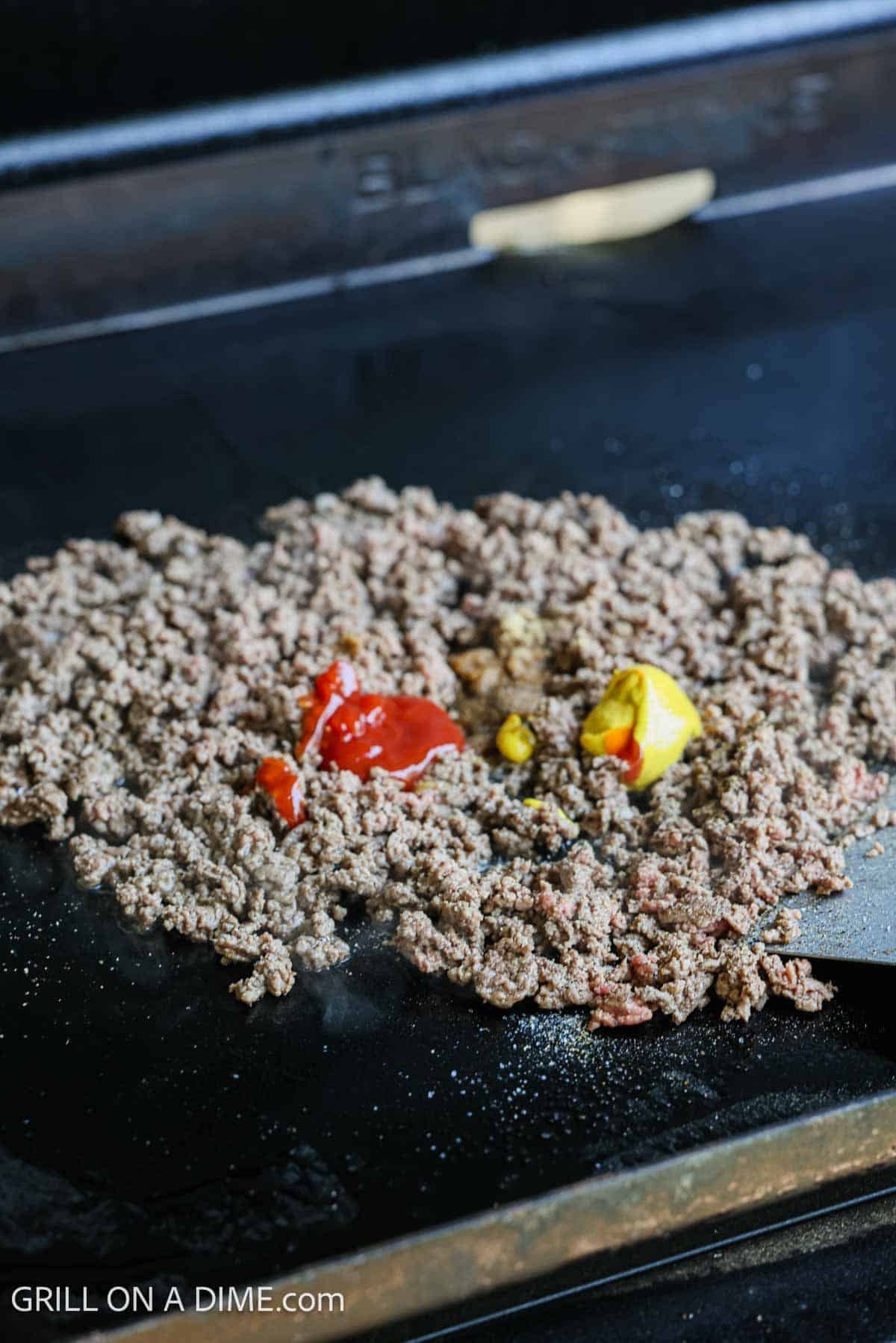 Cooked ground beef on the flat top griddle topped with ketchup and mustard.