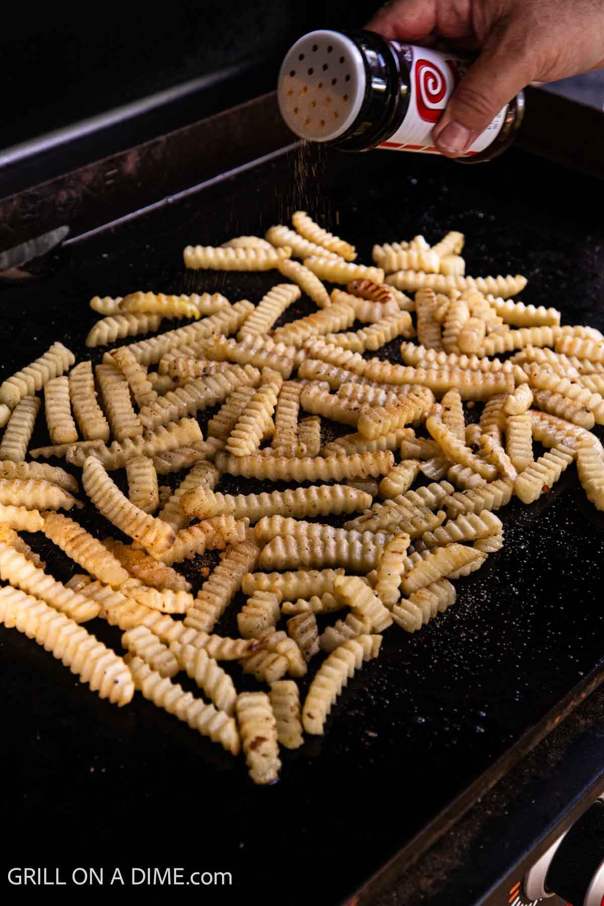 Adding seasoned salt to the french fries on the griddle. 
