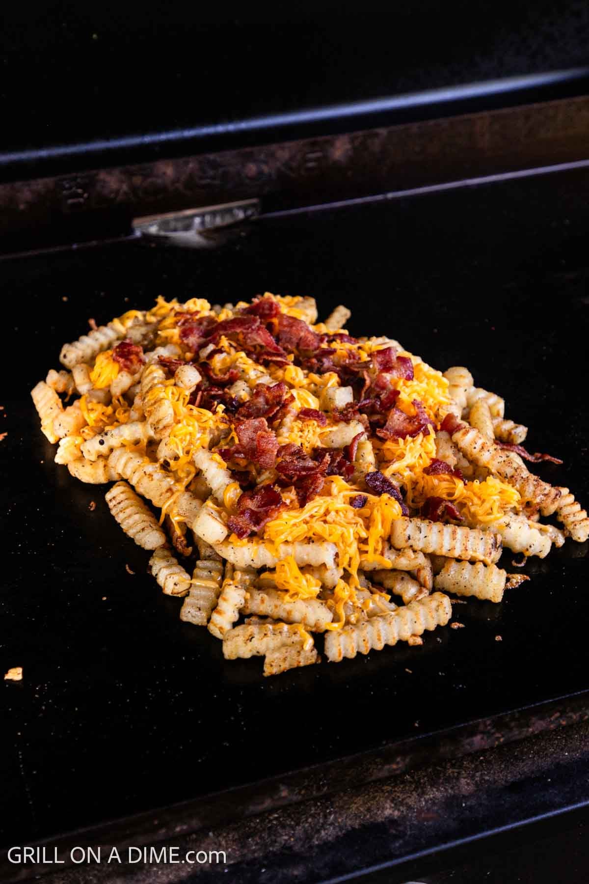 Topping the french fries with shredded cheese and chopped bacon. 