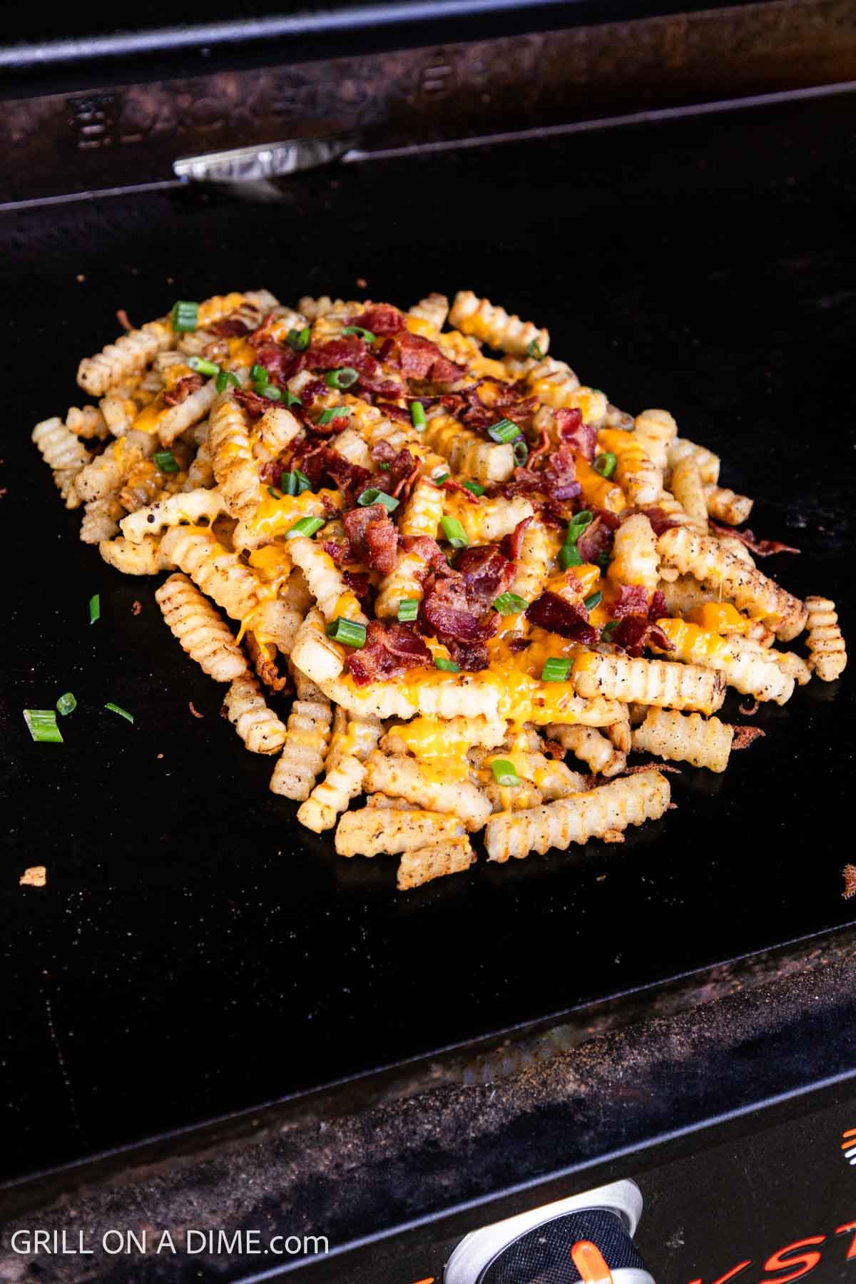 French fries topped with melted cheese, chopped bacon, and green onions on the griddle. 
