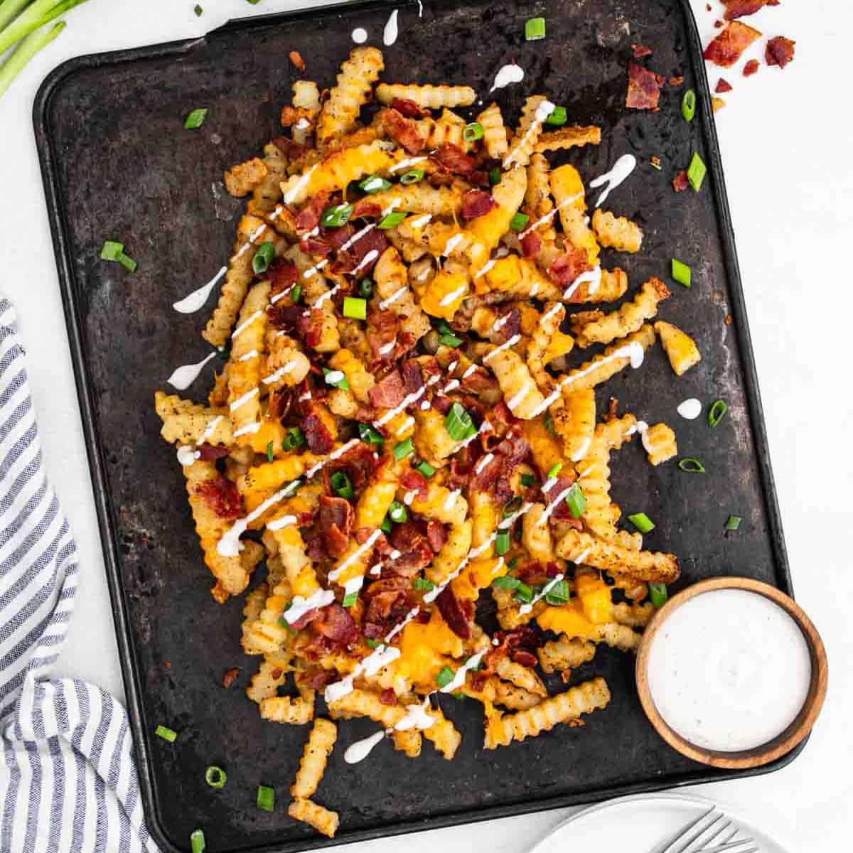 Loaded Cheese Fries on a black slate with a small bowl of ranch on the side.