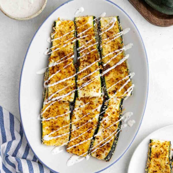 Parmesan crusted zucchini drizzled with ranch on a platter.