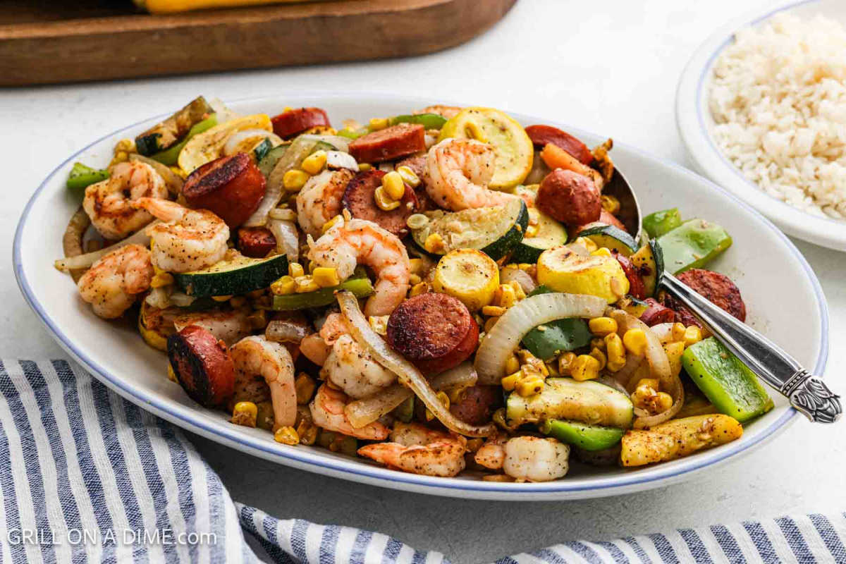 Cajun stir fry on a large oval platter with a plate of rice nearby. 