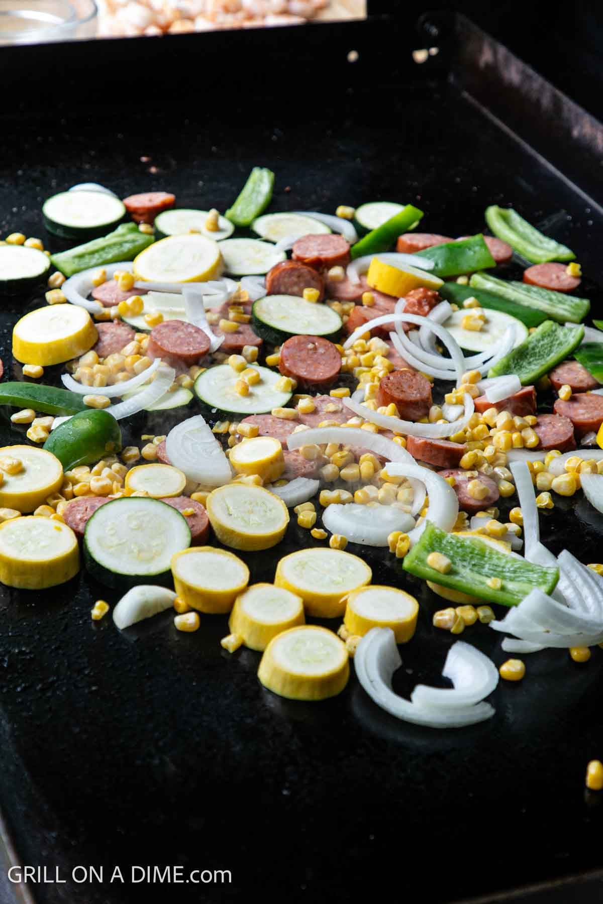 Squash, bell pepper, onions, zucchini, corn, and sausage cooking on the flat top griddle. 