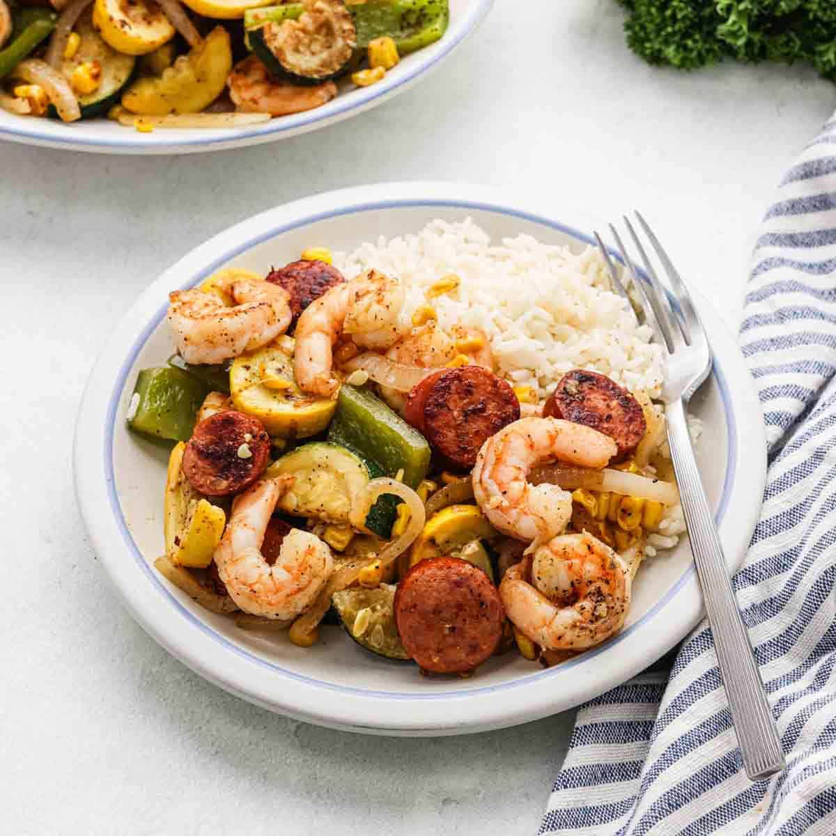 Shrimp, Sausage and Vegetable stir fry on a plate with a side of white rice.