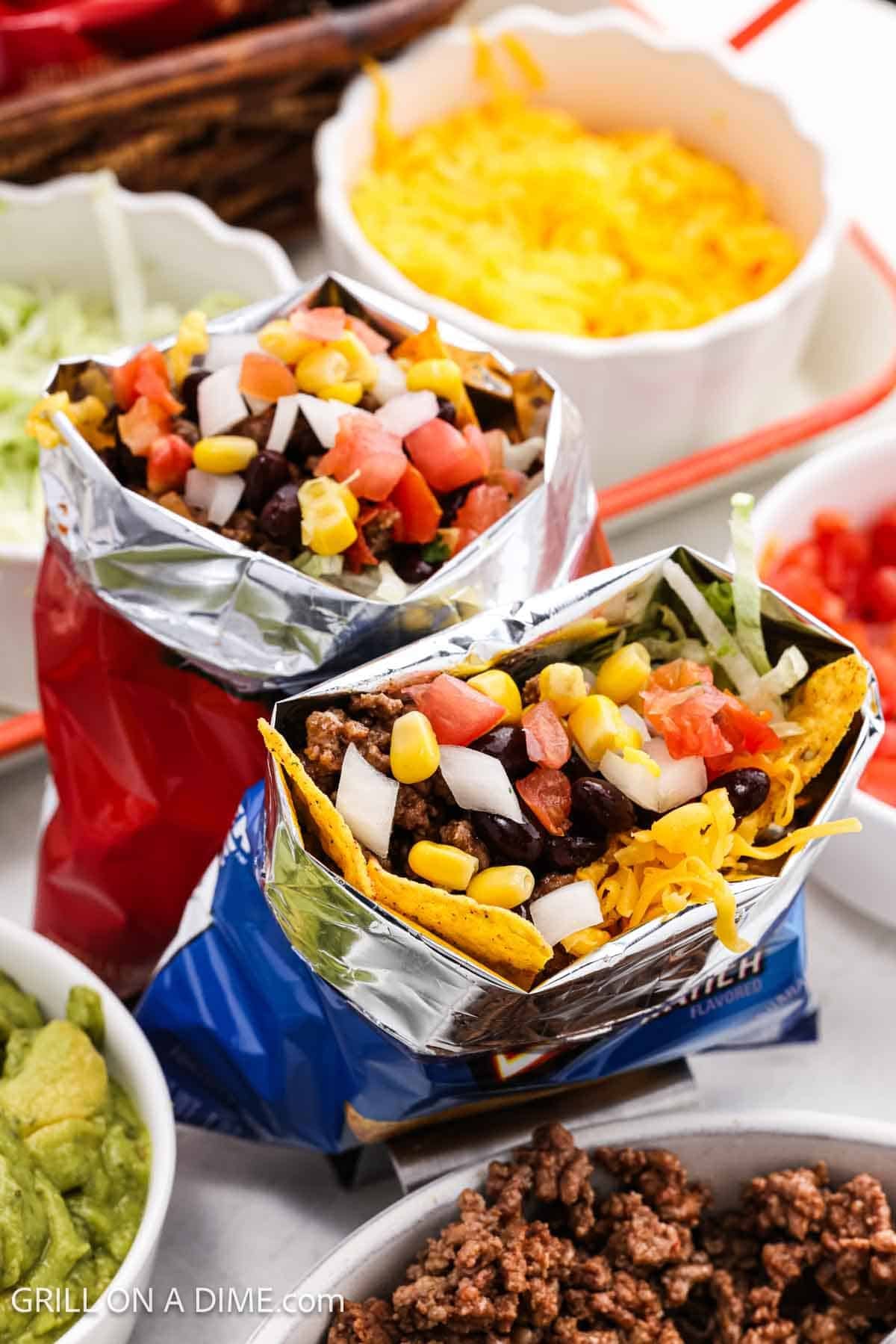 2 bags of Doritos in a taco stand filled with ground beef, chopped onions, corn, shredded cheese and pico.