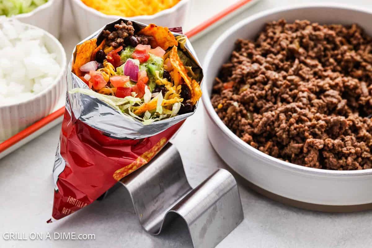 Walking Tacos in a taco stand with a large bowl of ground beef on the side.