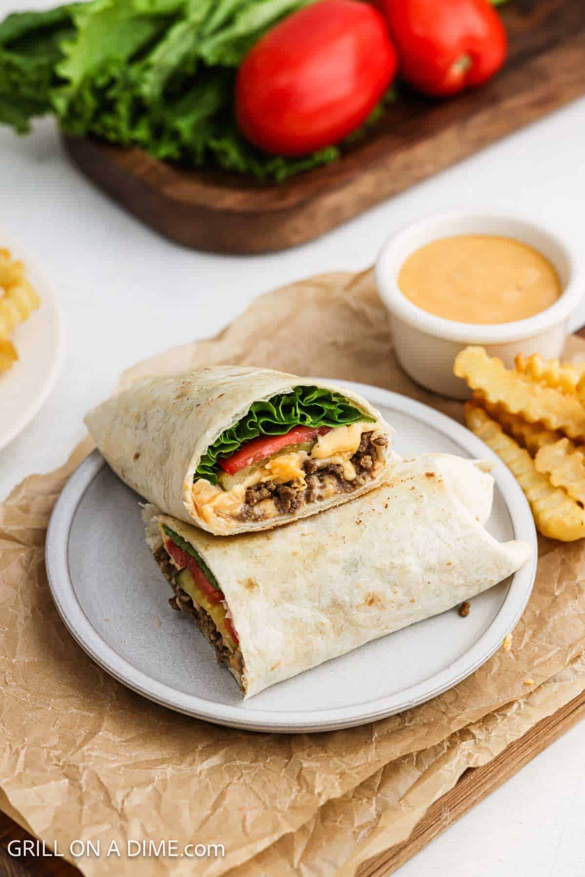Wrap cut in half and stacked on a plate with a side of dipping sauce and french fries.