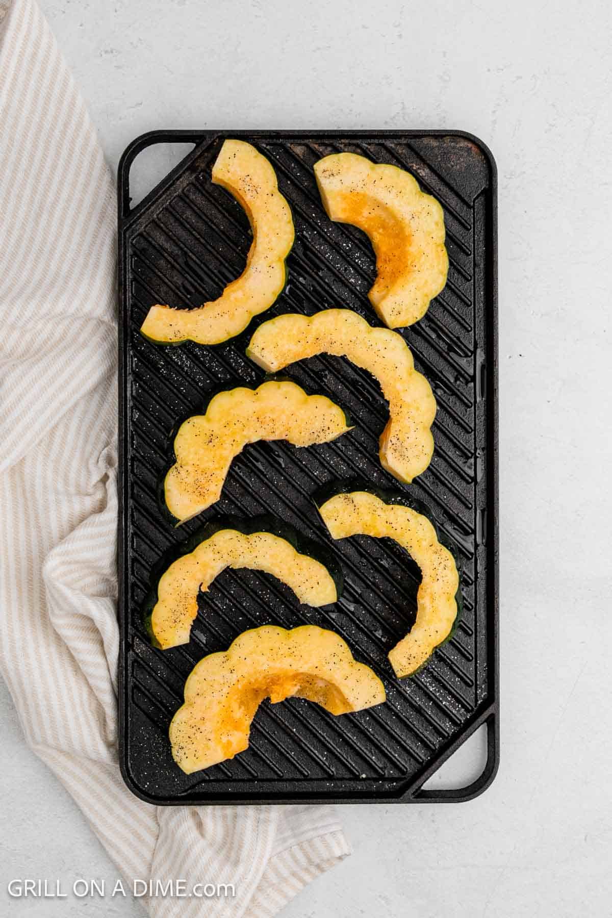 Seasoned sliced acorn squash on a grill.