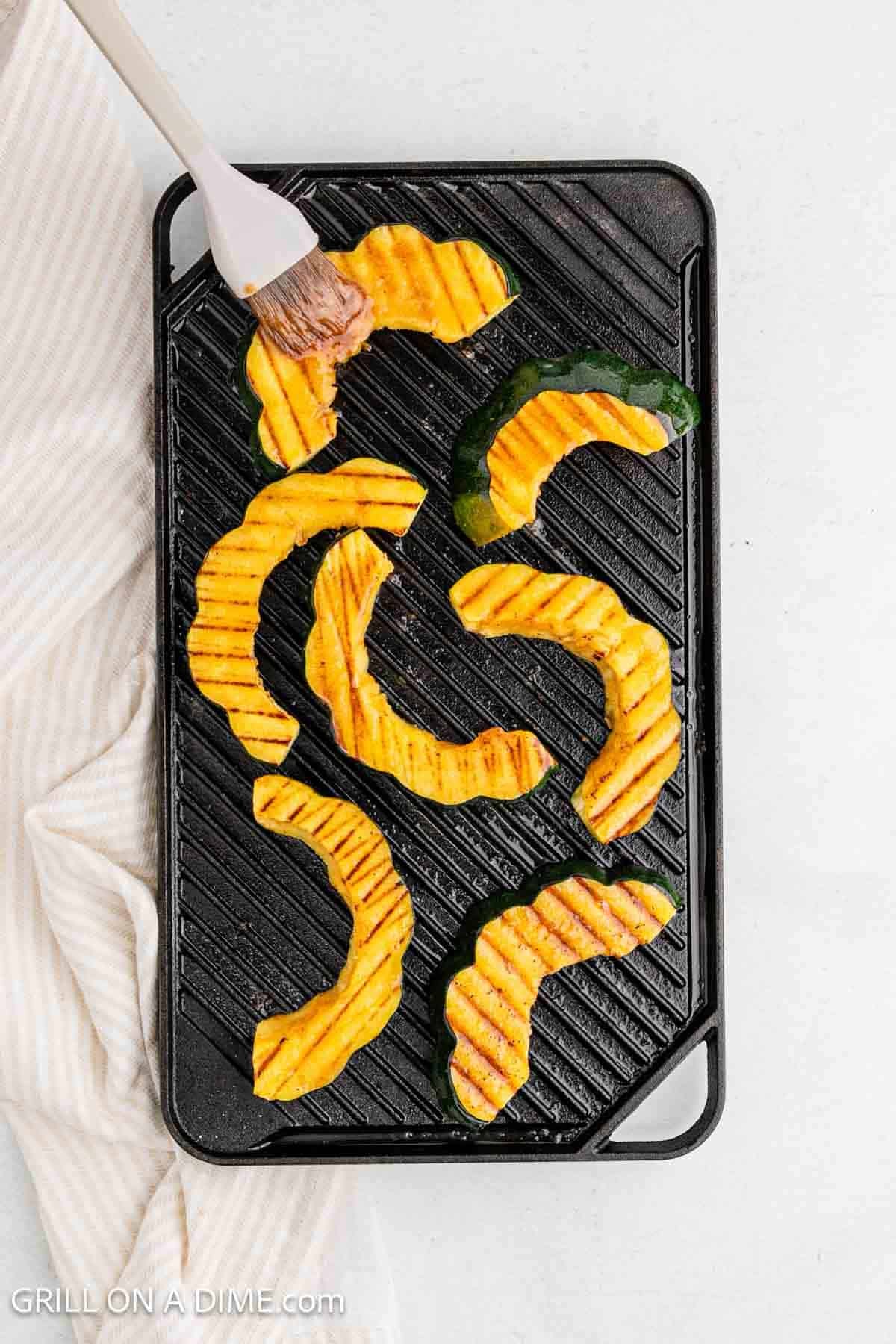 Brushing the glaze on the slices of acorn squash on a grill.