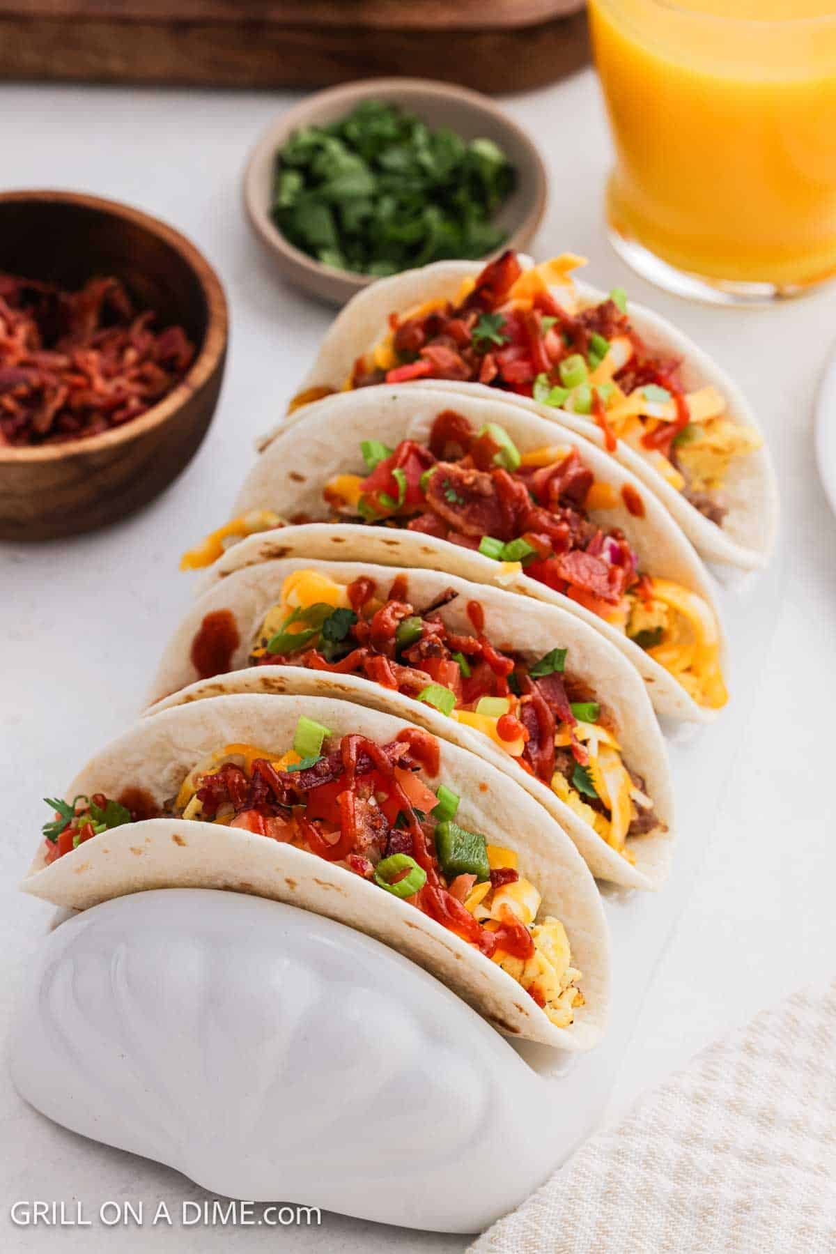 Tortillas filled with eggs, bacon, green onions and cheese in a taco stand. 