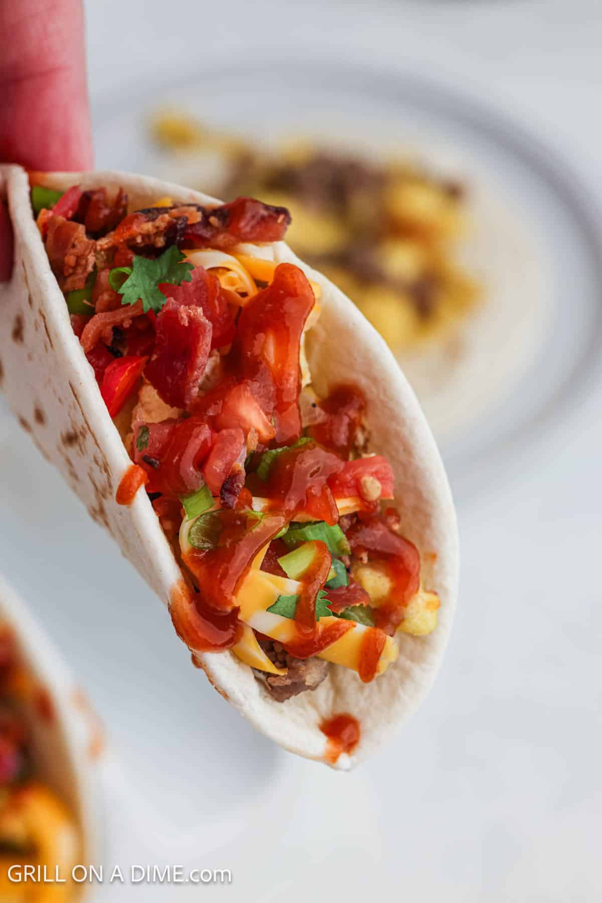 Close up of tortilla wrapped with eggs, cheese, sausage and veggies drizzled with hot sauce. 