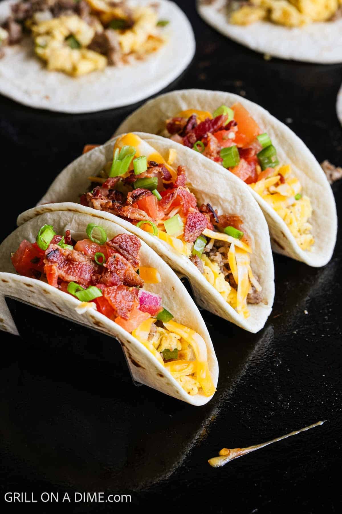Breakfast tacos on a taco stand on the flat top grill. 